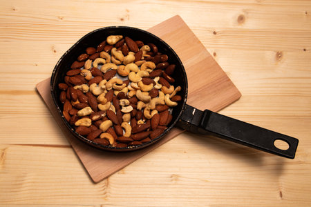 Roasted almonds and cashews in a pan on a wooden boardの写真素材