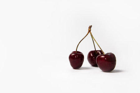 Three red cherries with stems on white backgroundの写真素材