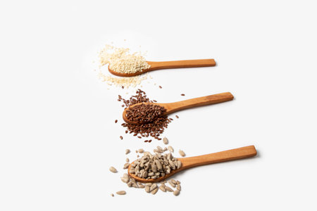 Sesame seeds flax seeds sunflower seeds in wooden spoons on white background
