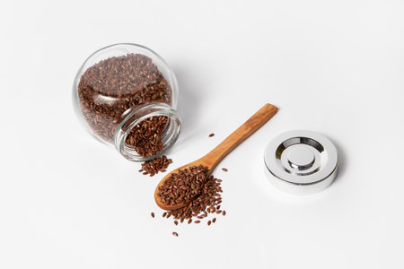 Glass jar and wooden spoon with flax seeds on white backgroundの写真素材