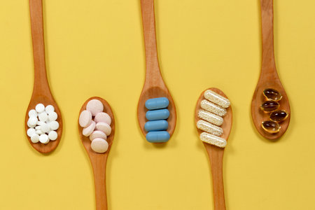 Top view of different vitamins and supplements in wooden spoons on yellow backgroundの写真素材