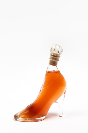 Glass bottle in the shape of a heel shoe with an orange drink on a white backgroundの写真素材