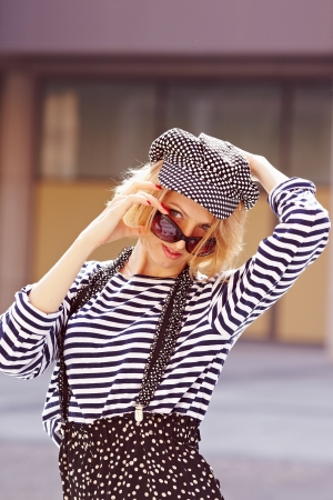 Beautiful girl in a vest and a plaid cap and suspenders on a city street.の写真素材