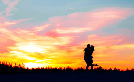 A silhouette of a girl approaching her beloved guy and hugs him against the backdropの写真素材