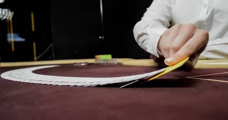 Dealer sitting in a casino at table while holding and distributing cardsの写真素材