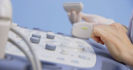 Doctor is making abdominal ultrasound for child girl using scanner machine in clinic, side view. Woman runs ultrasound sensor over patient tummy in clinic. Diagnostic examination of internal organs.の写真素材