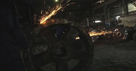 Working in a mask and headphones cleans joints angle grinder on metal parts blanks