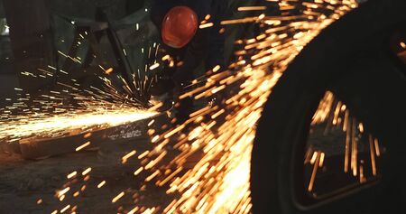 Working in a mask and headphones cleans joints angle grinder on metal parts blanks