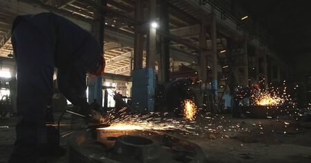 Working in a mask and headphones cleans joints angle grinder on metal parts blanks