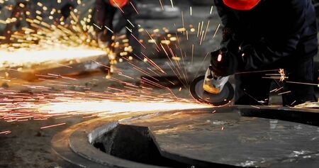 Working in a mask and headphones cleans joints angle grinder on metal parts blanks