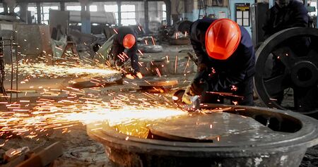 Working in a mask and headphones cleans joints angle grinder on metal parts blanks