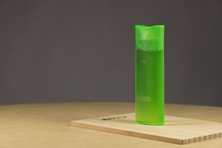Green plastic tube with shampoo isolated on brown background. On a wooden boardの写真素材