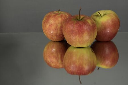 Three red apples on mirroring table on mirror gray background with reflection isolated close up. Mirror backgroundの写真素材