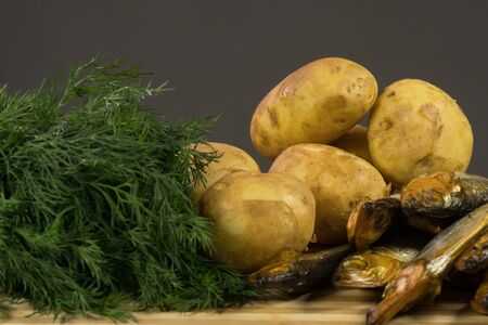 Young potatoes and smoked fish, young onions and dill on the board, a bottle of dark beerの写真素材