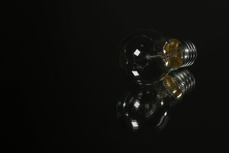 An old incandescent light bulb on black background over a mirrorの写真素材