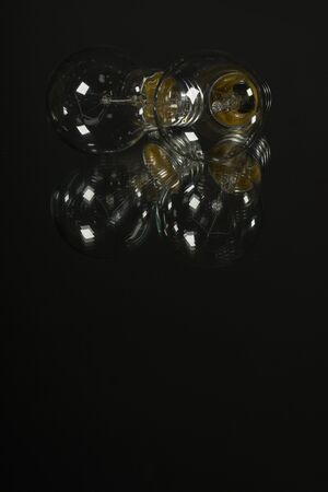An old incandescent light bulb on black background over a mirror