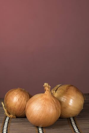 Three onions on bamboo board cutting, red backgroundの写真素材