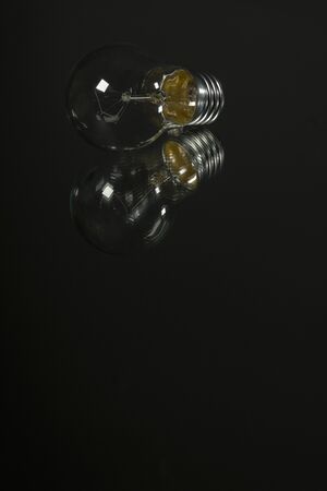 An old incandescent light bulb on black background over a mirrorの写真素材