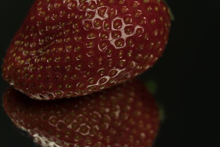 Macro shot of a strawberry. On a mirror black backgroundの写真素材
