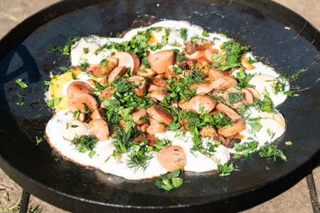 Scrambled eggs with sausage and herbs in a chunny pan in nature