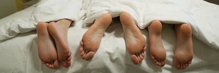 three pairs of legs in bed under a white blanket