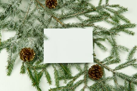 White card on the background of fir branches with cones and Christmas toys on a white wooden background. Mock up, copy spaceの写真素材