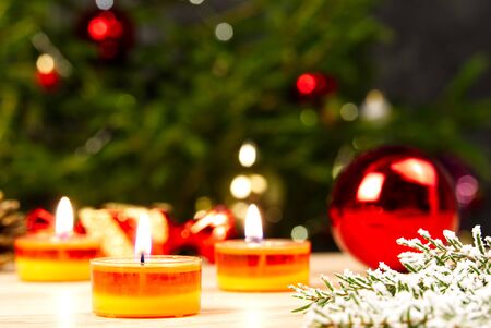 Burning candles and christmas decorations. Red balls for Christmas tree and fir twig on wooden floor with bokeh background. copy spaceの写真素材