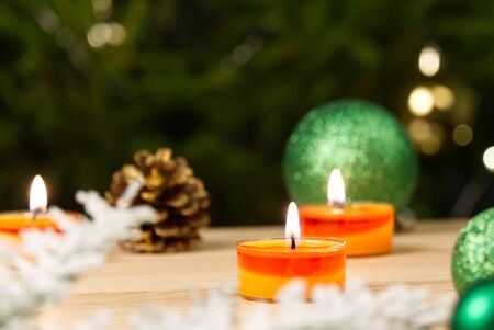 Burning candles and christmas decorations. Green balls for Christmas tree and fir twig on wooden floor with bokeh background. Copy spaceの写真素材