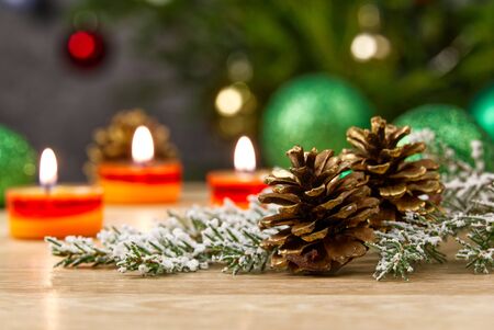 Burning candles and christmas decorations. Green balls for Christmas tree and fir twig on wooden floor with bokeh background. Copy spaceの写真素材