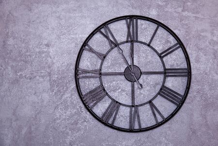 Vintage wall clock with roman numerals on the wall. gray stucco wall. Clock shows five to twelve 11:55の写真素材