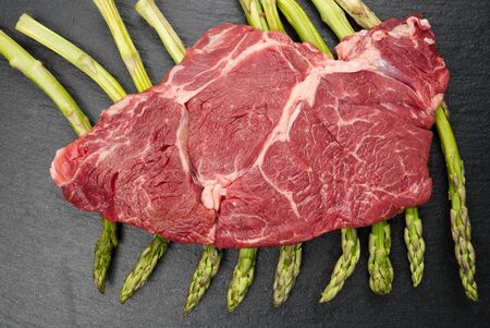 Raw rib eye steak with spices and vegetables. Ingredients for restaurant meal. Fresh meat, salt, rosemary, thyme, chilli, cherry tomatoes, garlic on black stone. Food background, copy space, top viewの写真素材