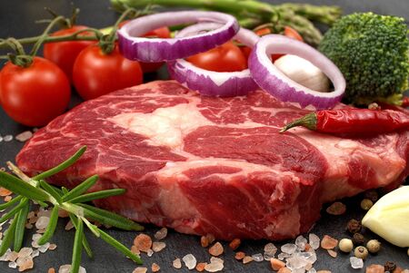 Raw rib eye steak with spices and vegetables. Ingredients for restaurant meal. Fresh meat, salt,...