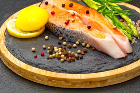fresh raw salmon steaks with pepper corns, salt, lemon and olive oil on black background. Healthy food, diet concept. Preparation for cooking fish with spices.の写真素材