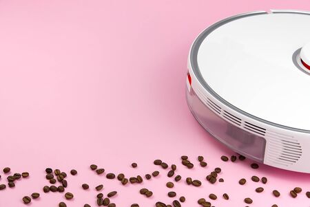 white robot vacuum cleaner on a pink background with coffee grains. concept of cleaning with a robot cleanerの写真素材