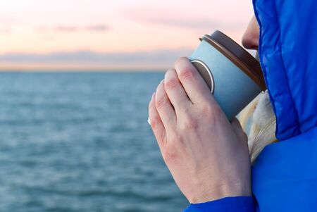 beautiful girl drinks coffee from a takeaway cup, looking at the sunset. Sunset on the Baltic Sea...