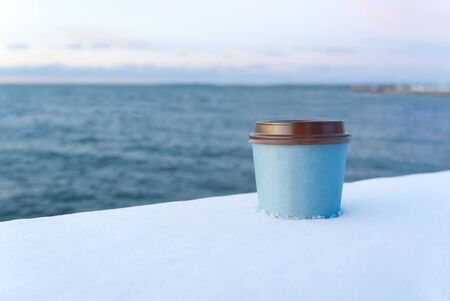 take away coffee with sea background at winter time. winter snow take away coffee cup sunset at seaの写真素材