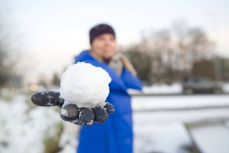 a hand in a black leather glove holds a snowball with a backdrop of a snowy field. soft focusの写真素材
