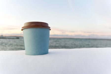 take away coffee with sea background at winter time. winter snow take away coffee cup sunset at sea .の写真素材