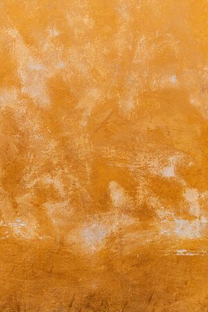 Texture of an old orange plastered street wall. old wall with peeling paint, scratched stained...