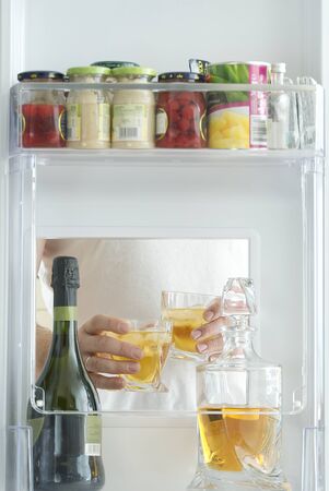 open hatch of a mini bar in a modern refrigerator. home mini bar in the fridge. a man took two glasses with alcohol from the counter, view from the refrigerator.の写真素材