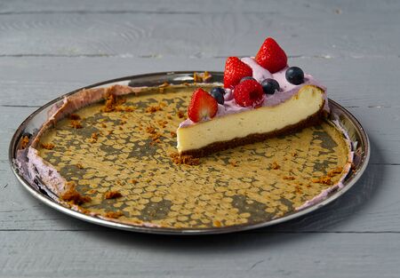 Last slice of home made Cheesecake with berries on plate on grey wooden background.