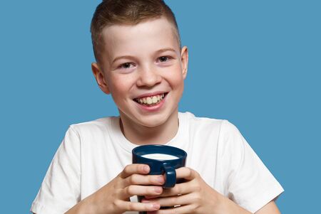 Happy Boy with blue mug of Milk Isolated on blue Background. Smiling boy holding blue cup with milk....