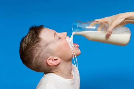 Happy Boy drinking Milk from bottle Isolated on Blue Background. Milk got by the boys mouthの写真素材