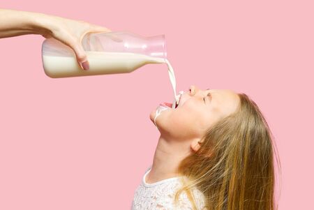 Happy Girl drinking Milk from bottle Isolated on Pink Background. Milk got by the girls mouthの写真素材