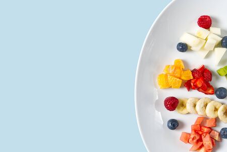 Fresh fruit salad on white plate. Mixed fruit in white plate healthy food style. Useful fruit salad of fresh fruits and berries on light blue backgroundの写真素材