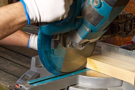 Closeup of professional cabinet makers working with electric circular saw at woodworking workshop....