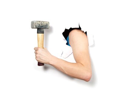 close-up hand with hammer through a torn white paper, isolated. hand holding Hammer close-up sledgehammer through hole in white paper.の写真素材