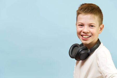 Smiling young handsome boy on a blue background in headphones. concept of baby radio, dj, singer or karaoke. happiness be music everywhere.の写真素材