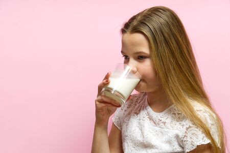 girl with pigtails and milk mustache drinks milk on pink background.の写真素材