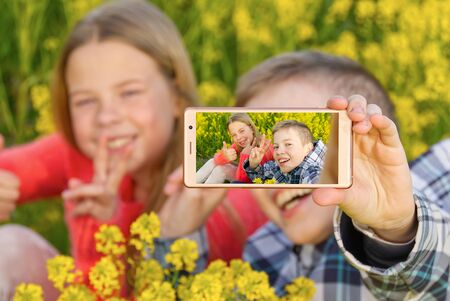 Happy smiling kids making self portrait on smartphone in meadow. young boy and girl making selfie on...